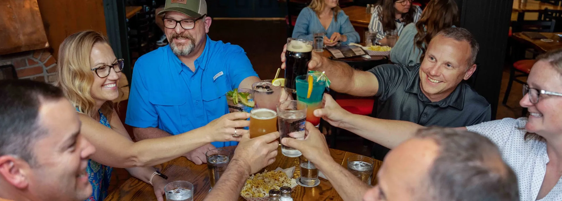 Group of guests raising a toast with beers around a pub table